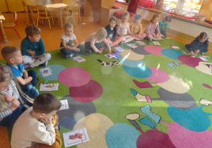 Grupa dzieci siedzi na dywanie, każde z dzieci ma przed sobą ułożony obrazek przedstawiający misie.